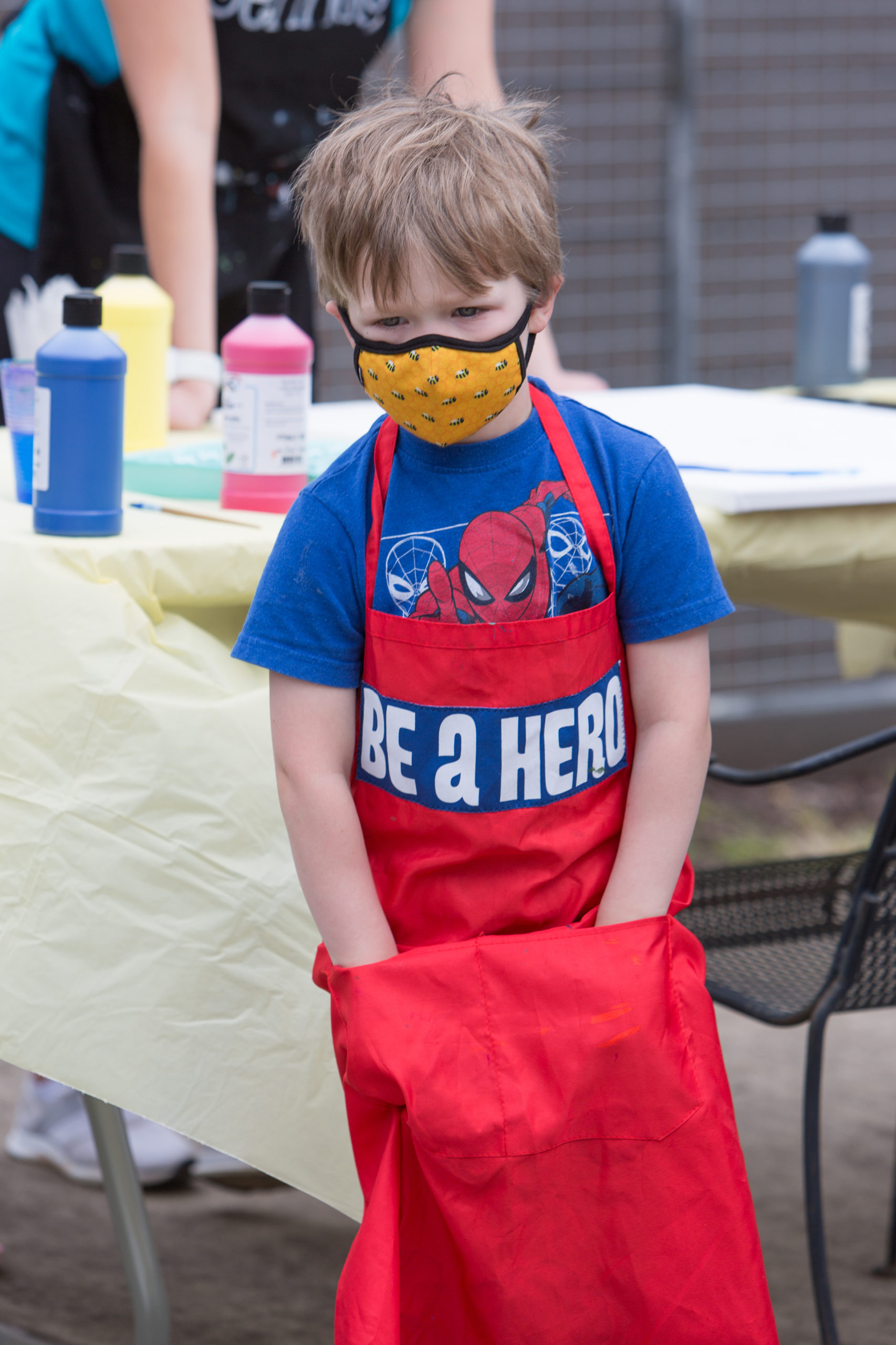 A boy is wearing a face mask an apron saying Be A Hero and a spiderman t-shirt