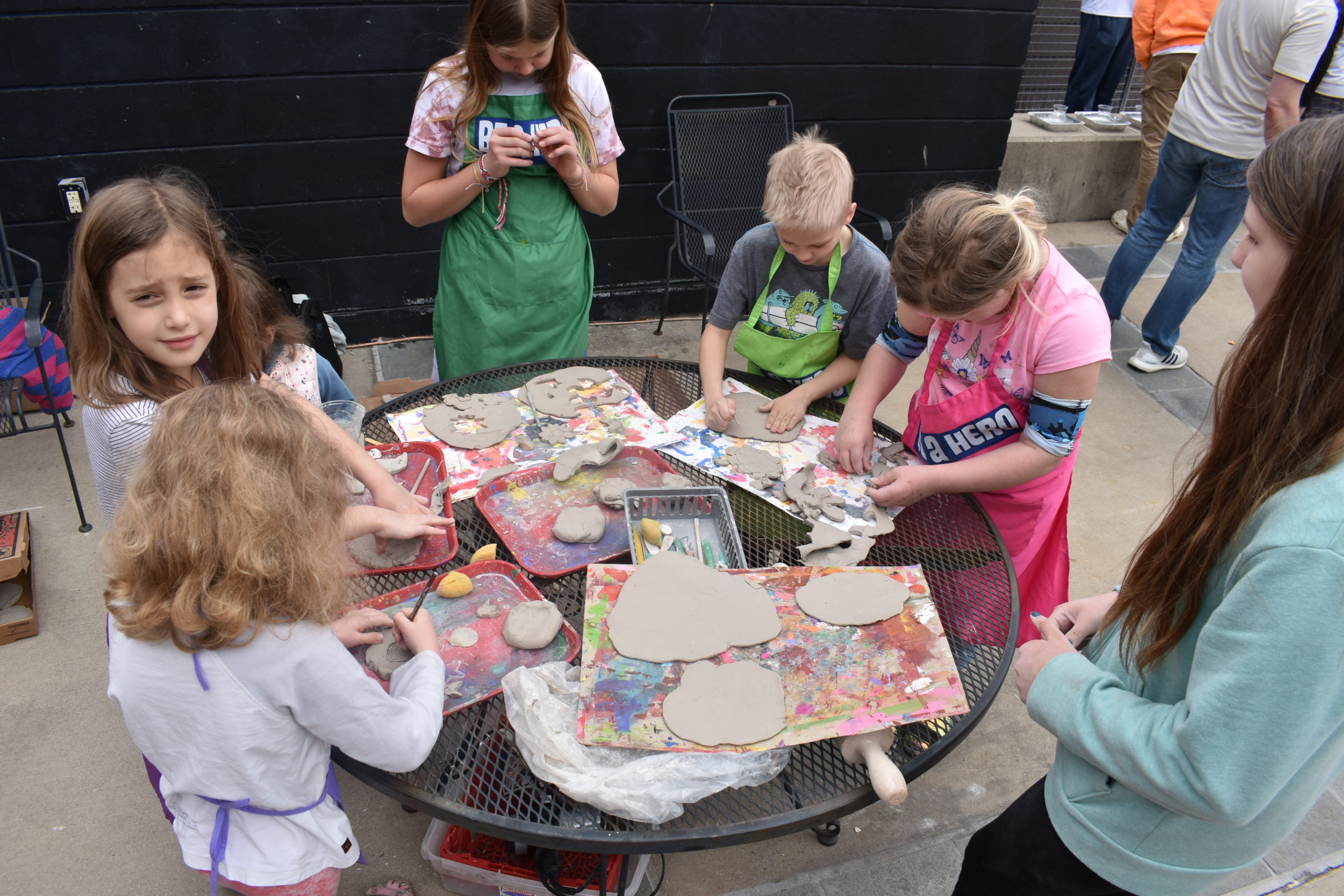 Six children are standing around a table molding pieces of clay