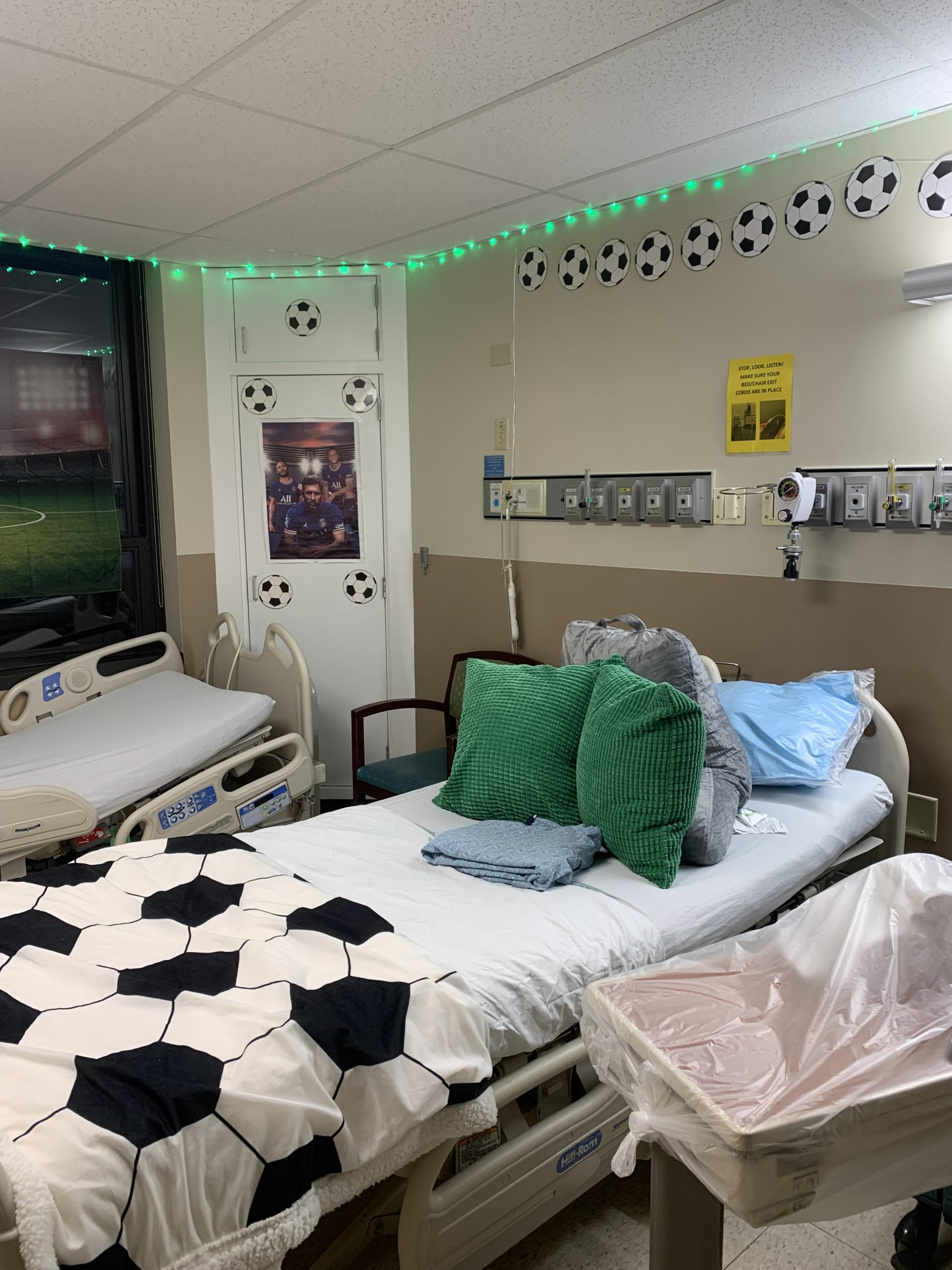 A hospital bed with a soccer ball quilt and two green pillows