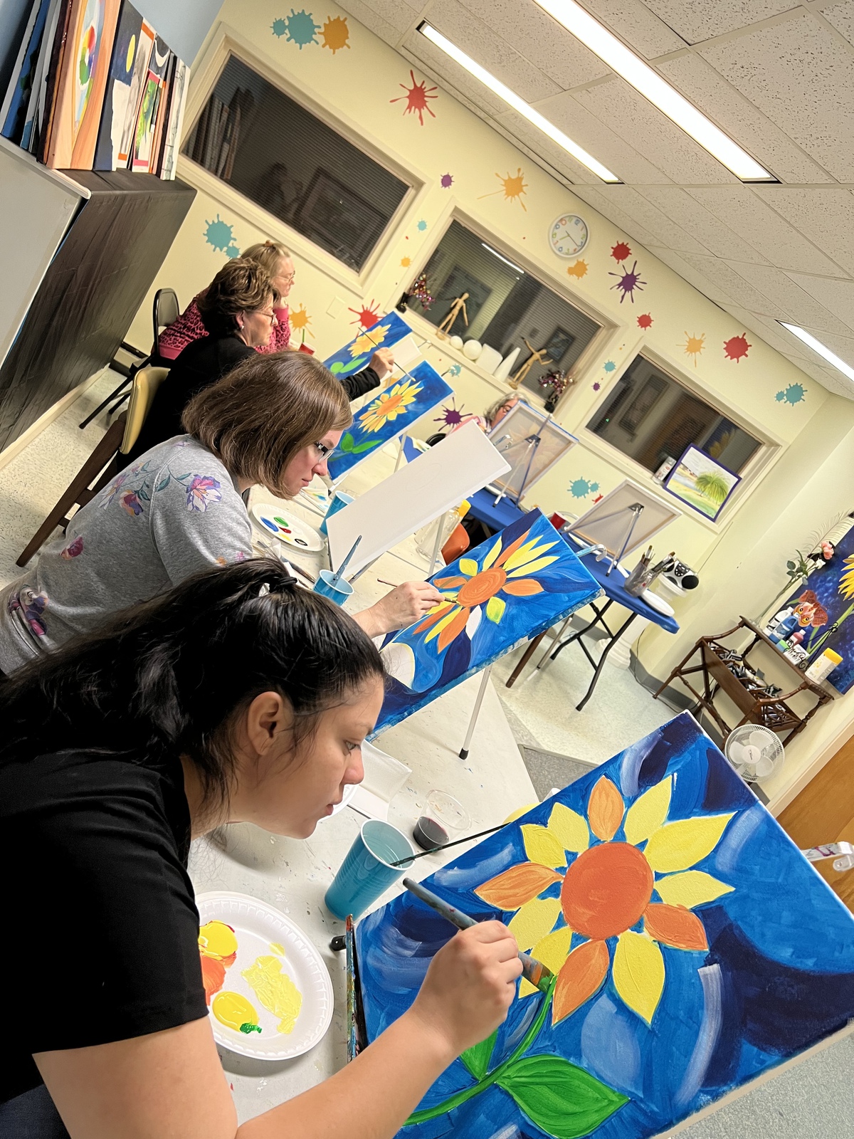 Women sitting at a table each one is painting a flower on a canvas