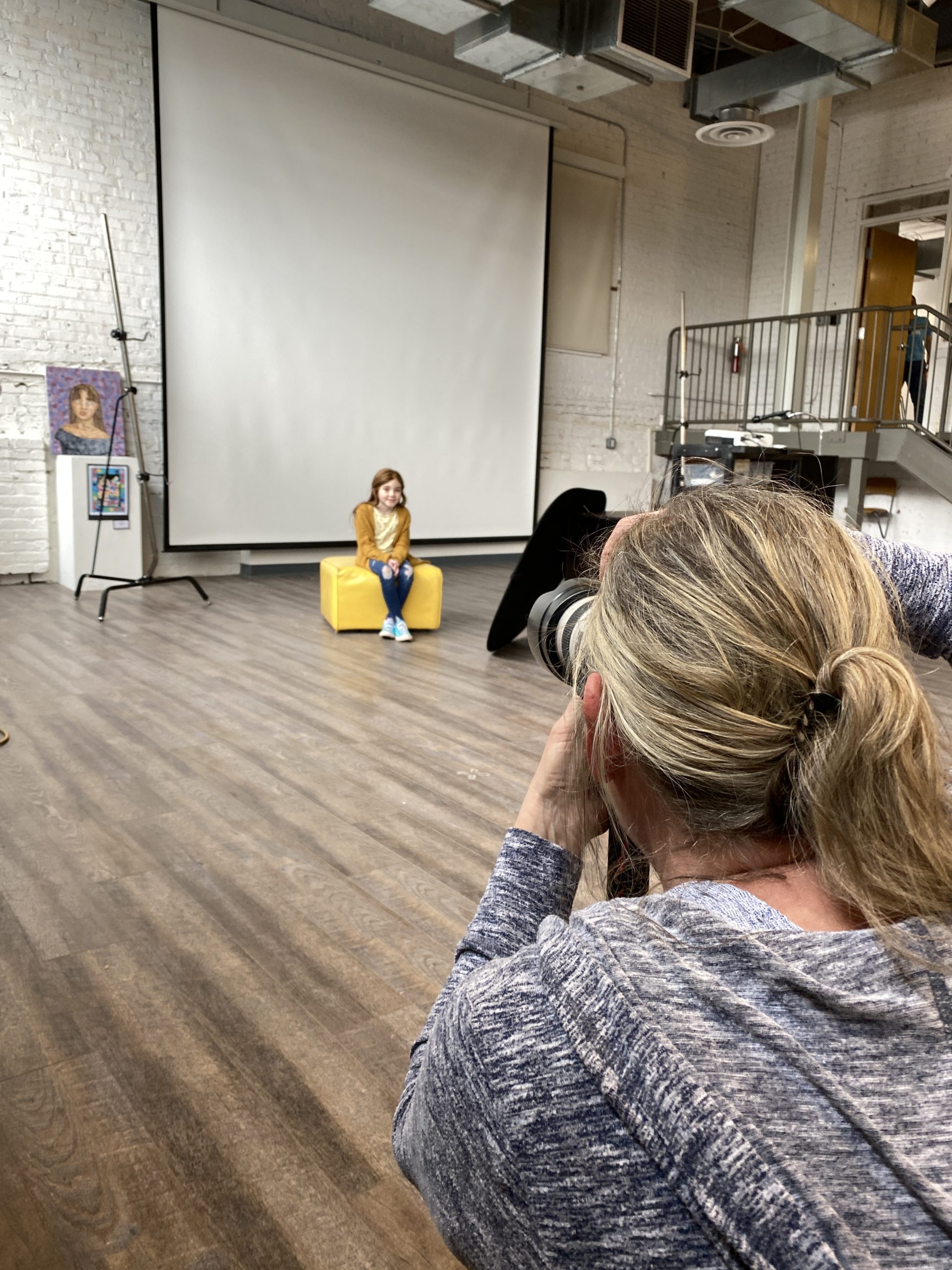 A woman taking a photo of a girl sitting for a portrait