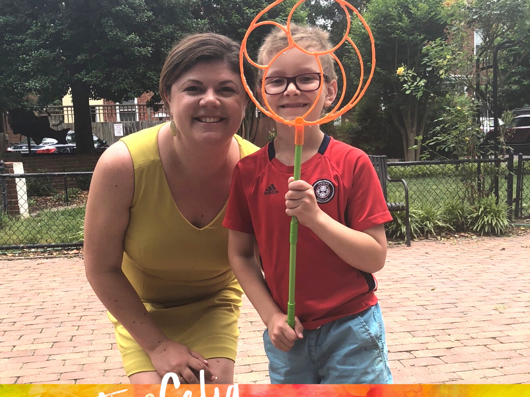 A woman and a child standing in a park The boy is holding a giant bubble wand