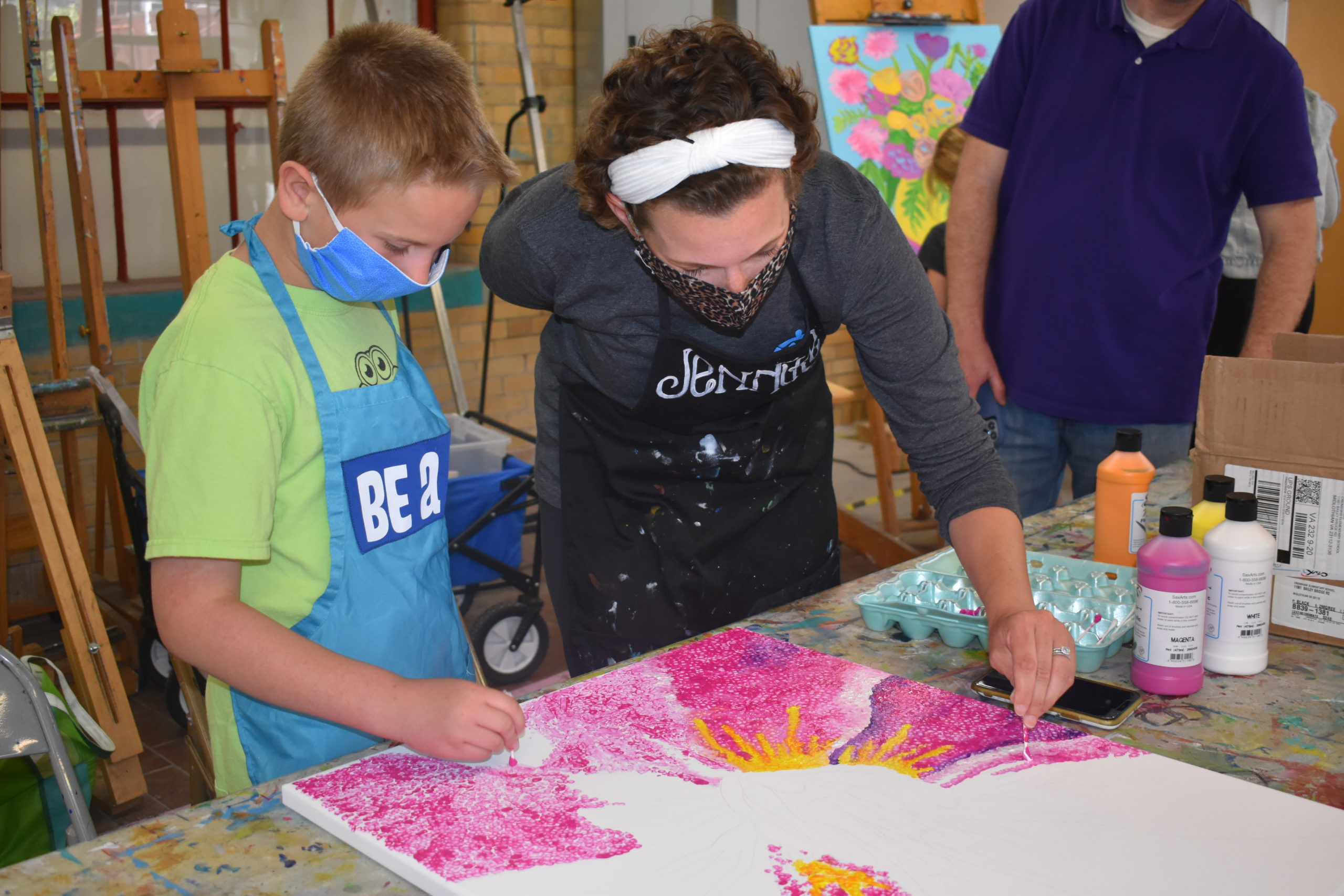 An artist helps a boy paint pink dots on a large canvas