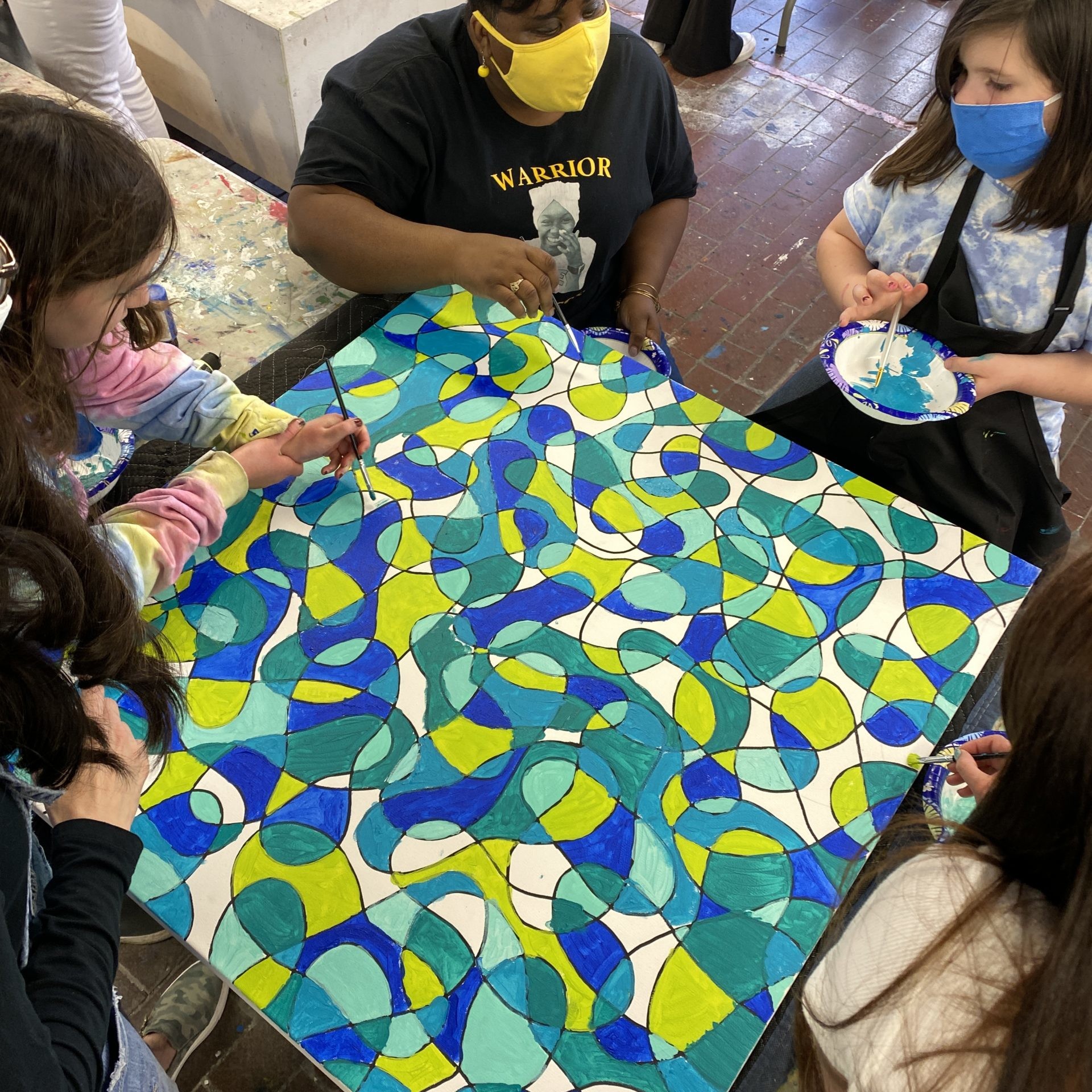 Four chlidren help a woman paint a large canvas with blue and green paints