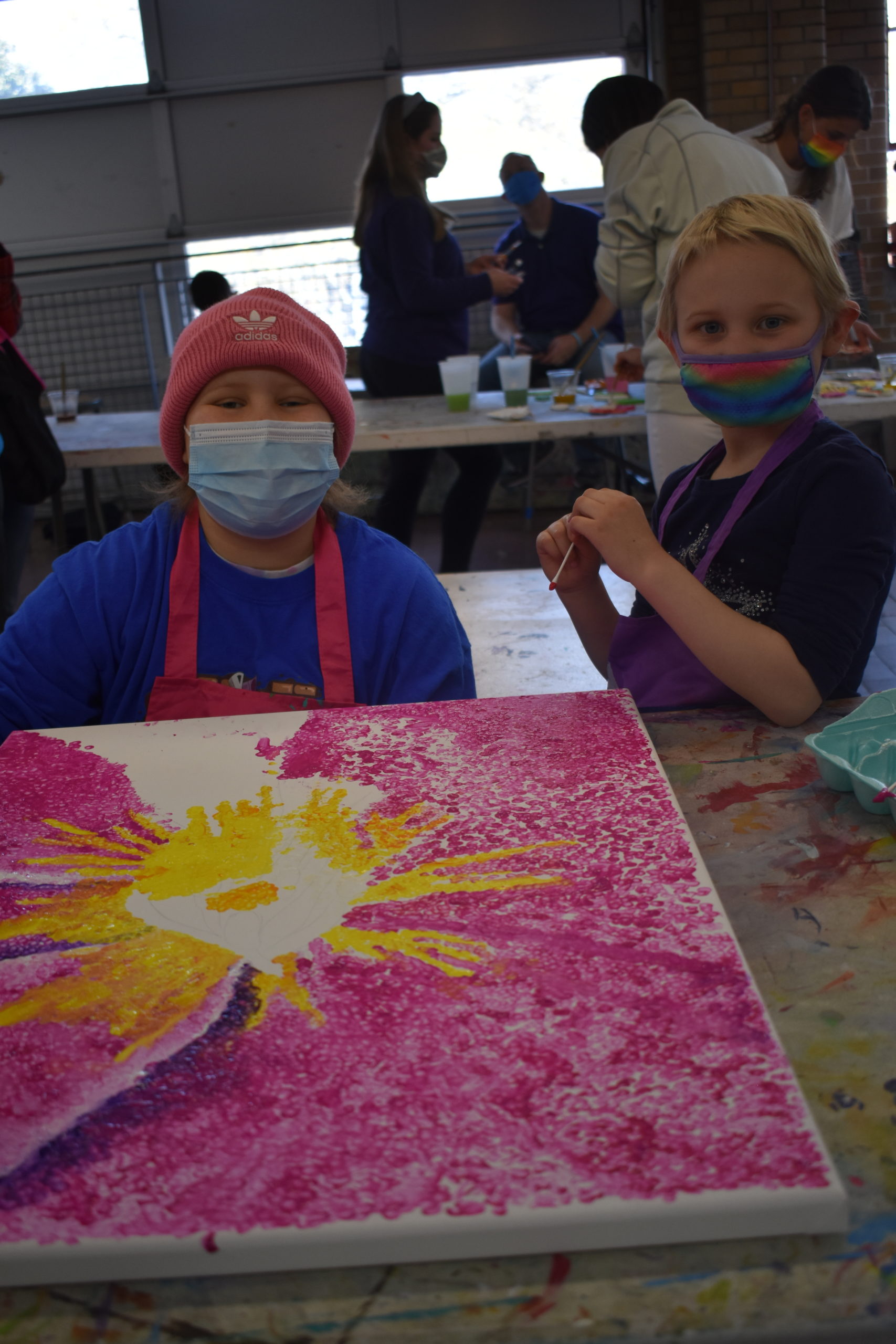 Two children are showing their painting of a large pink flower