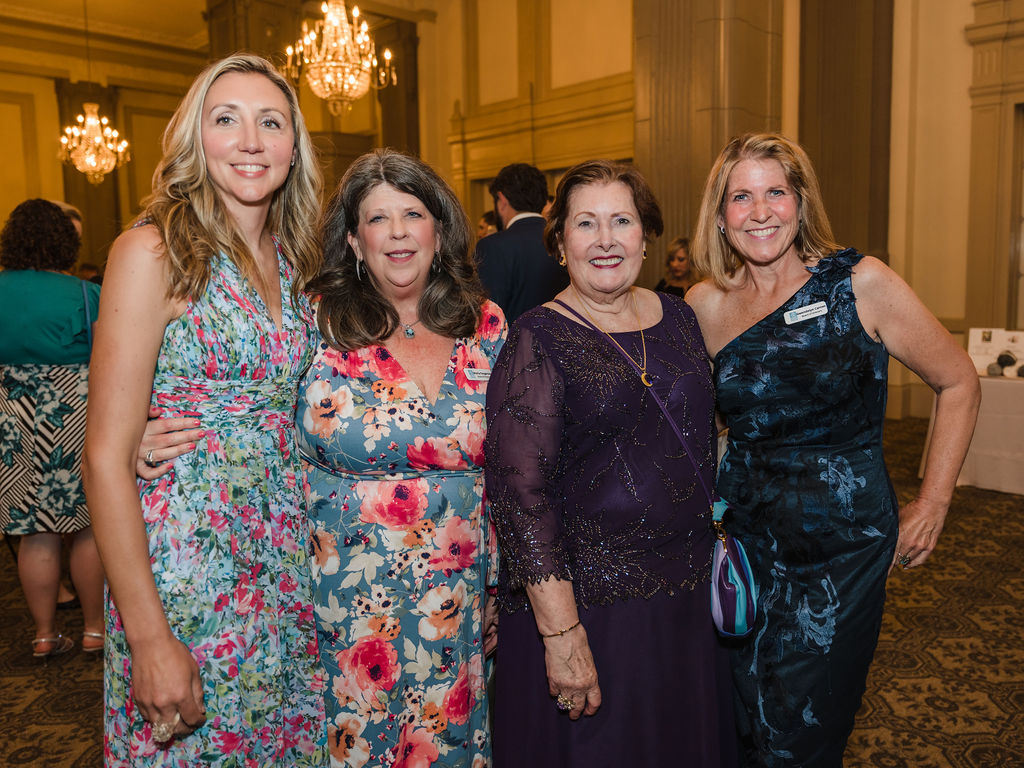 Four women posing for a photo and standing in a hotel ballroom