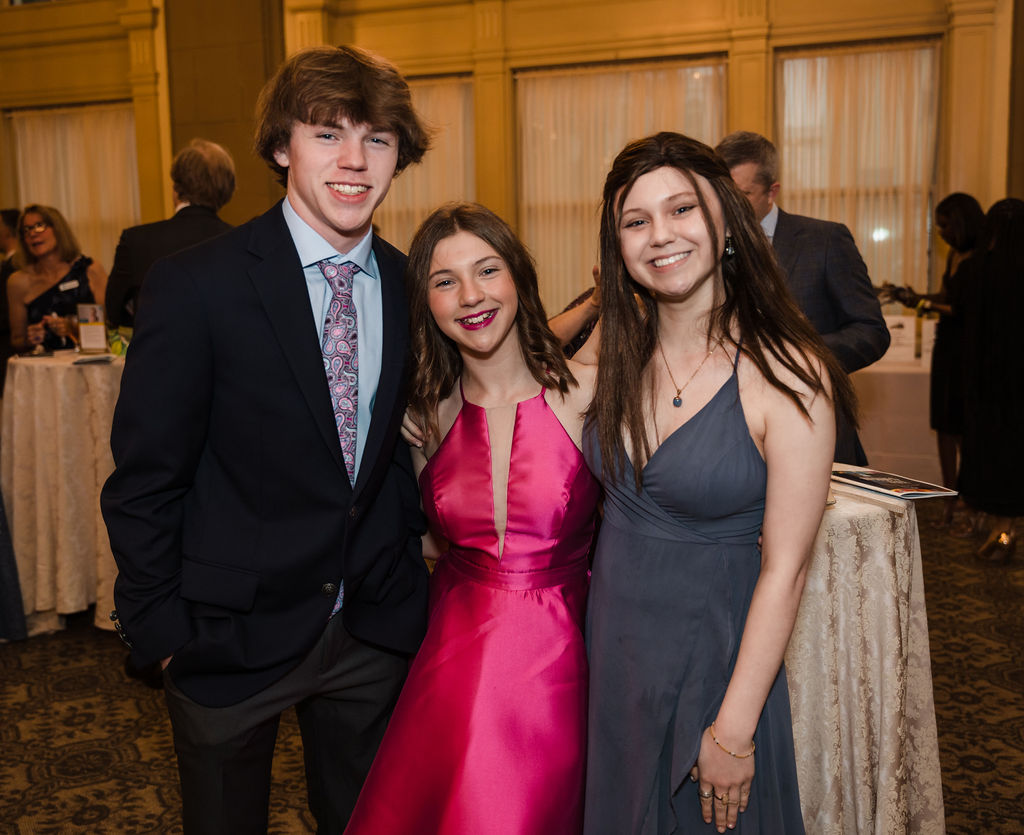 Three teenagers standing in a ballroom dressed for a gala
