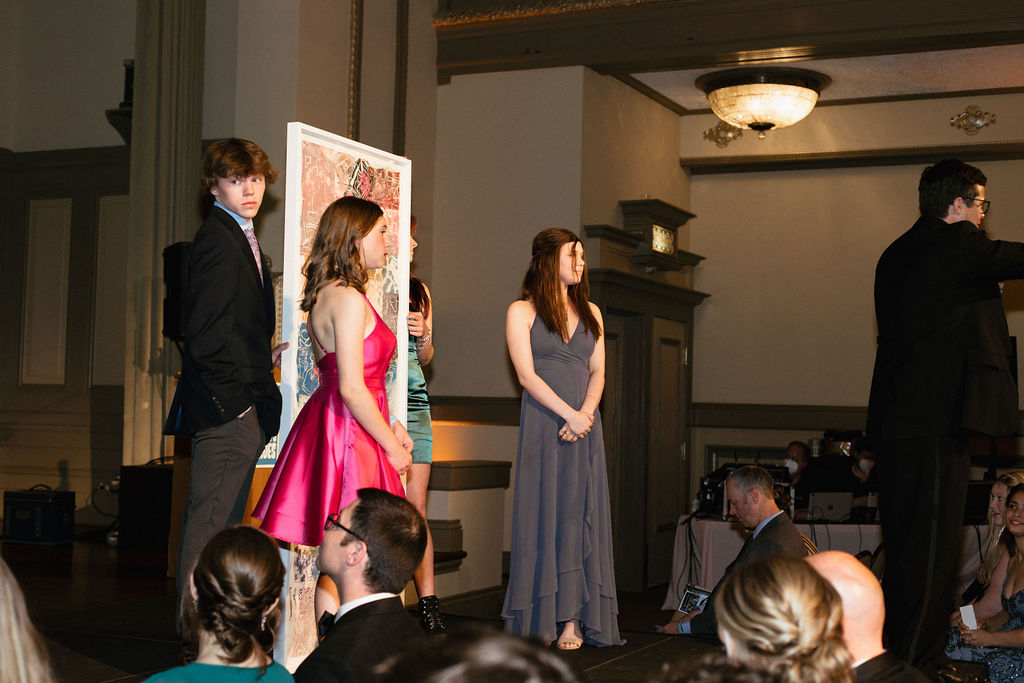 Teens standing on a stage They are holding a large painting