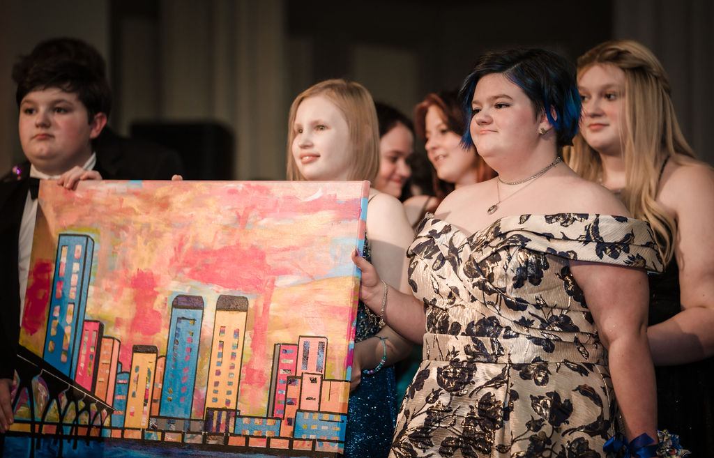 A group of teens standing on the stage together holding up a painting