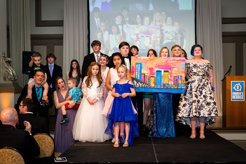 A group of children, teenagers and their parents standing on stage together They are holding up a large painting of the Richmond skyline