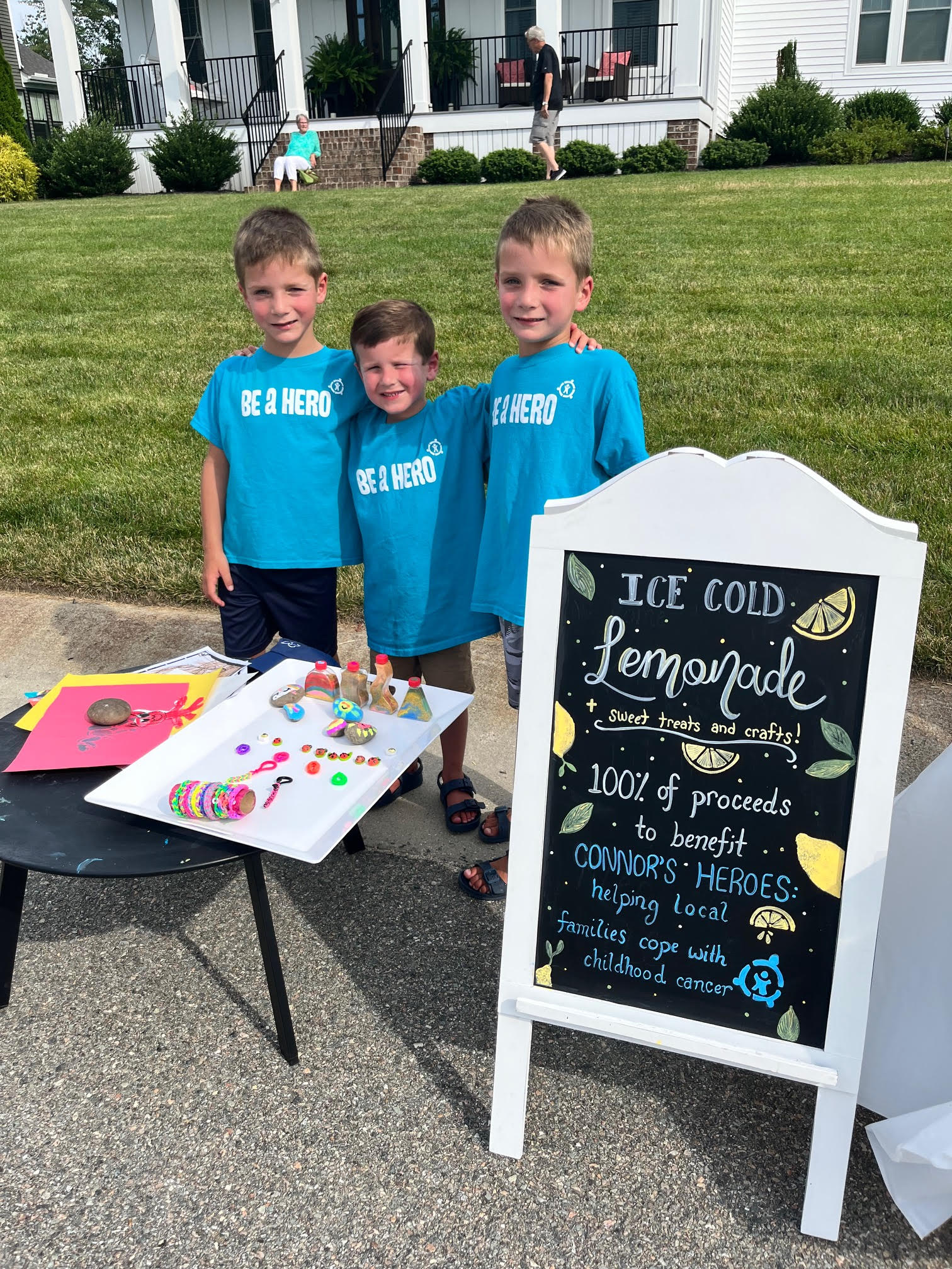 Three children standing on the sidewalk with a sign for their lemonade stand