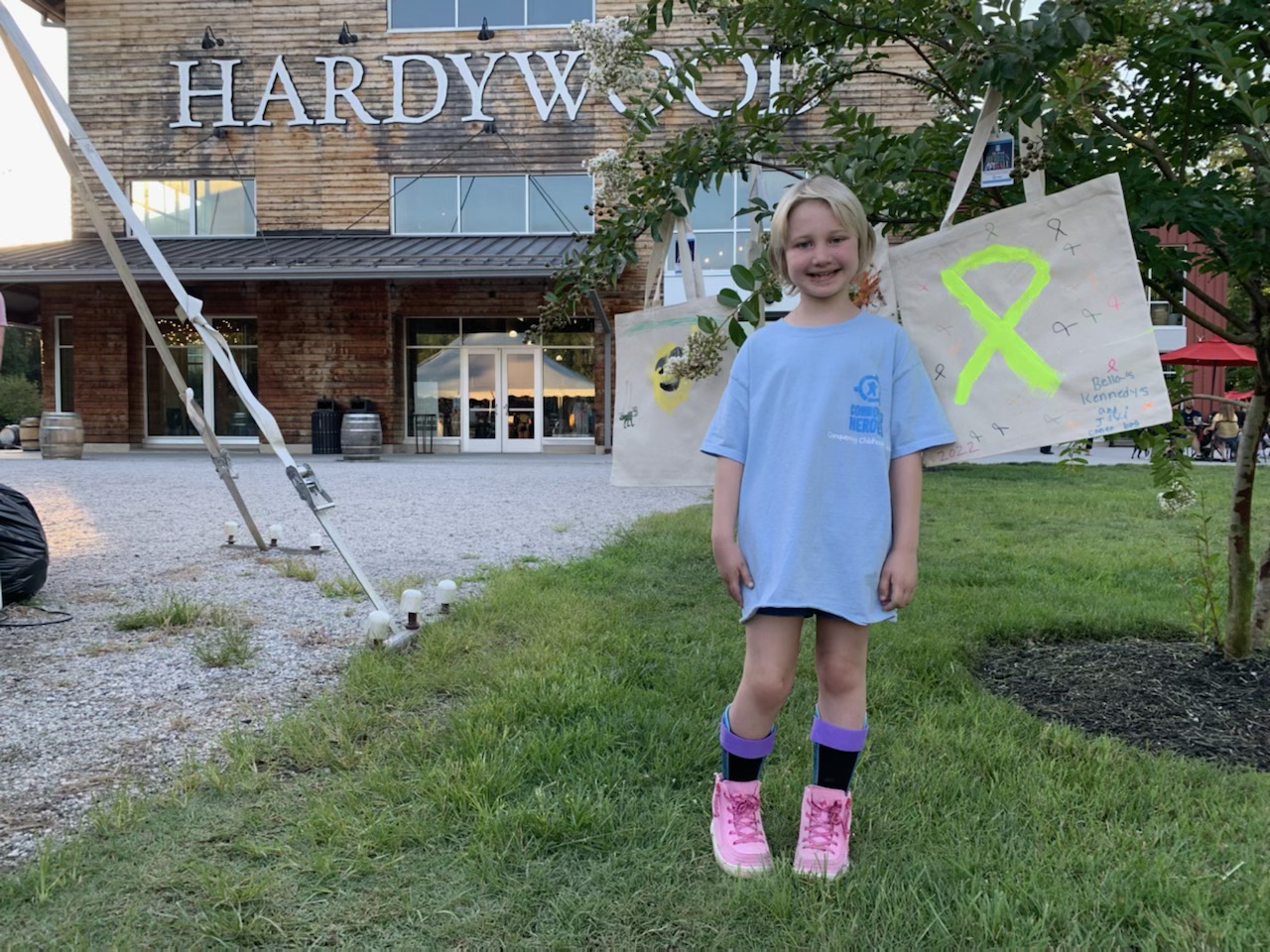 A girl is standing next to a tree in front of Hardywood