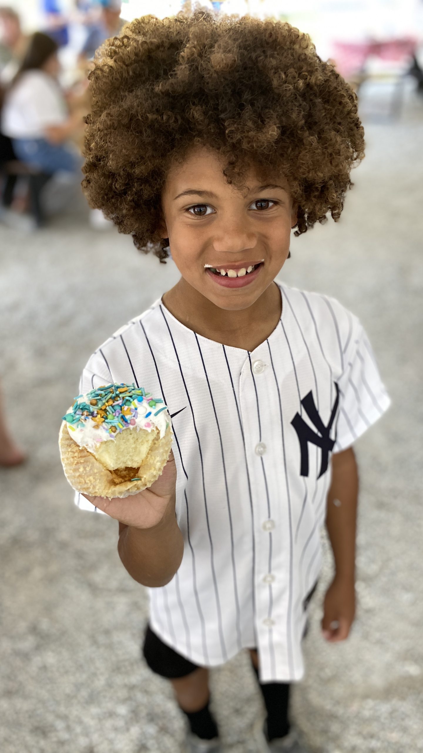 A child is holding up a cupcake he decorated with sprinkles