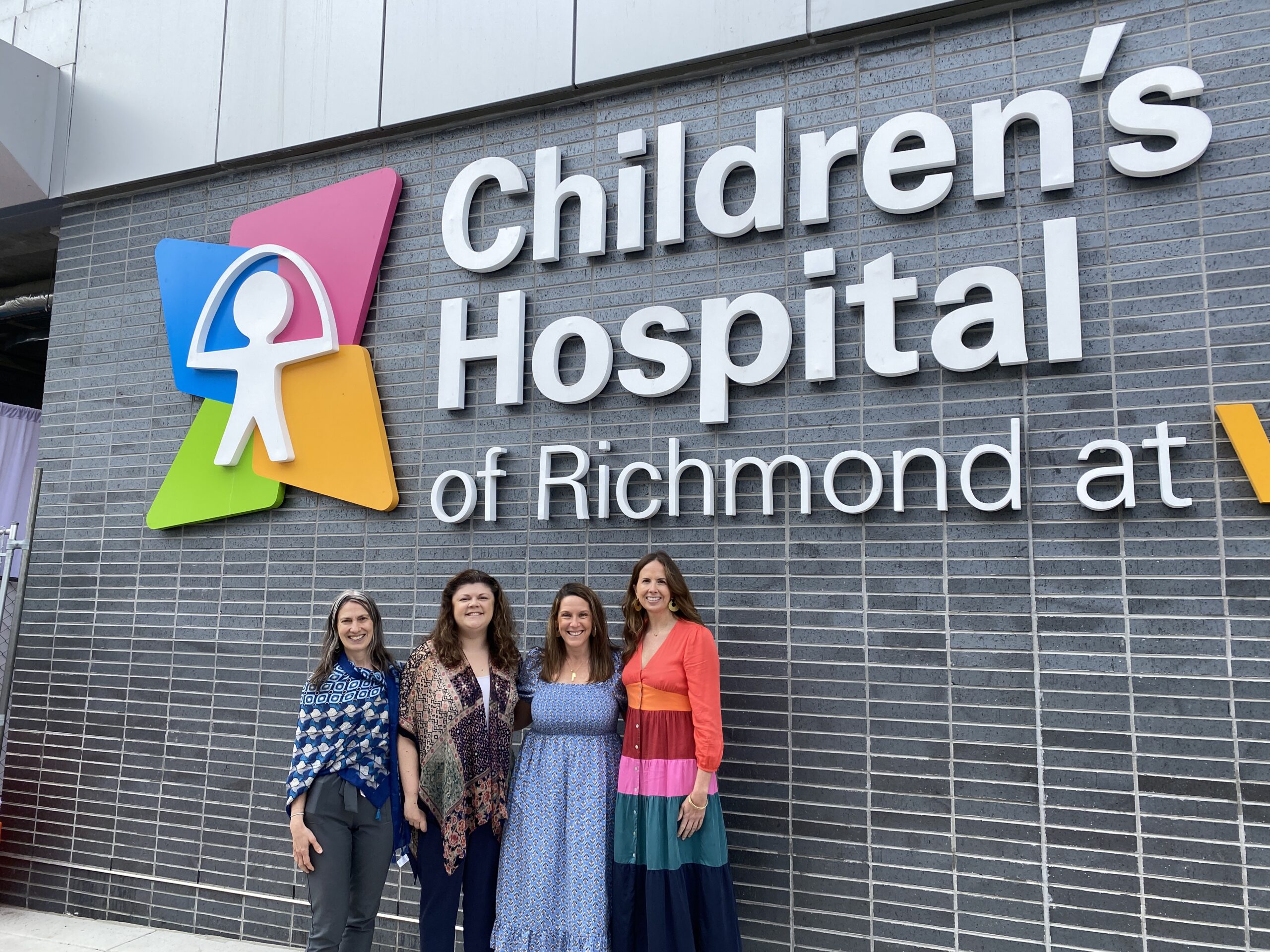 Ceci, Celia, Anne-Randolph and Erin are standing in front of the large sign for the Children's Hospital of Richmond at VCU