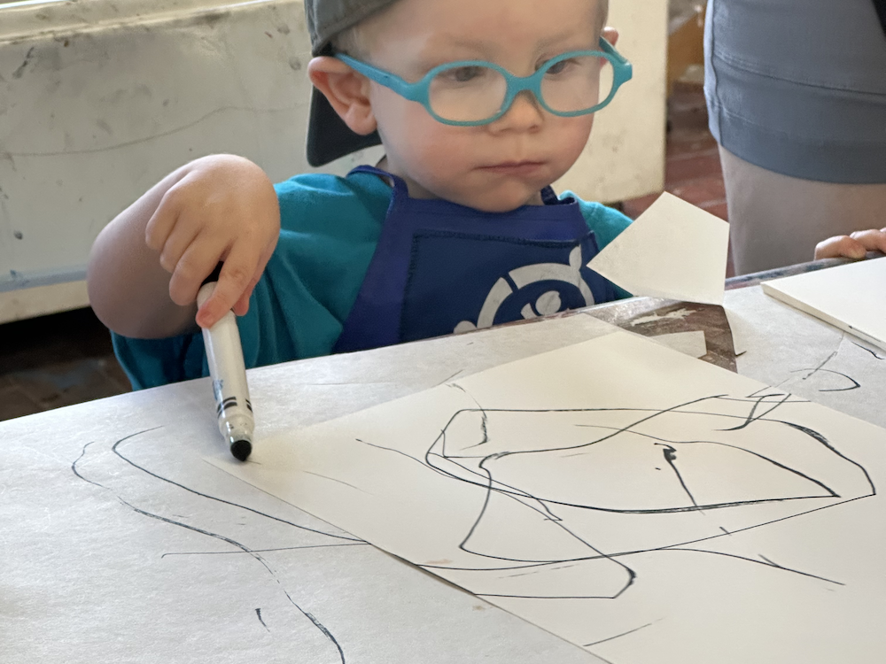 A boy wearing blue glasses and drawing with a marker