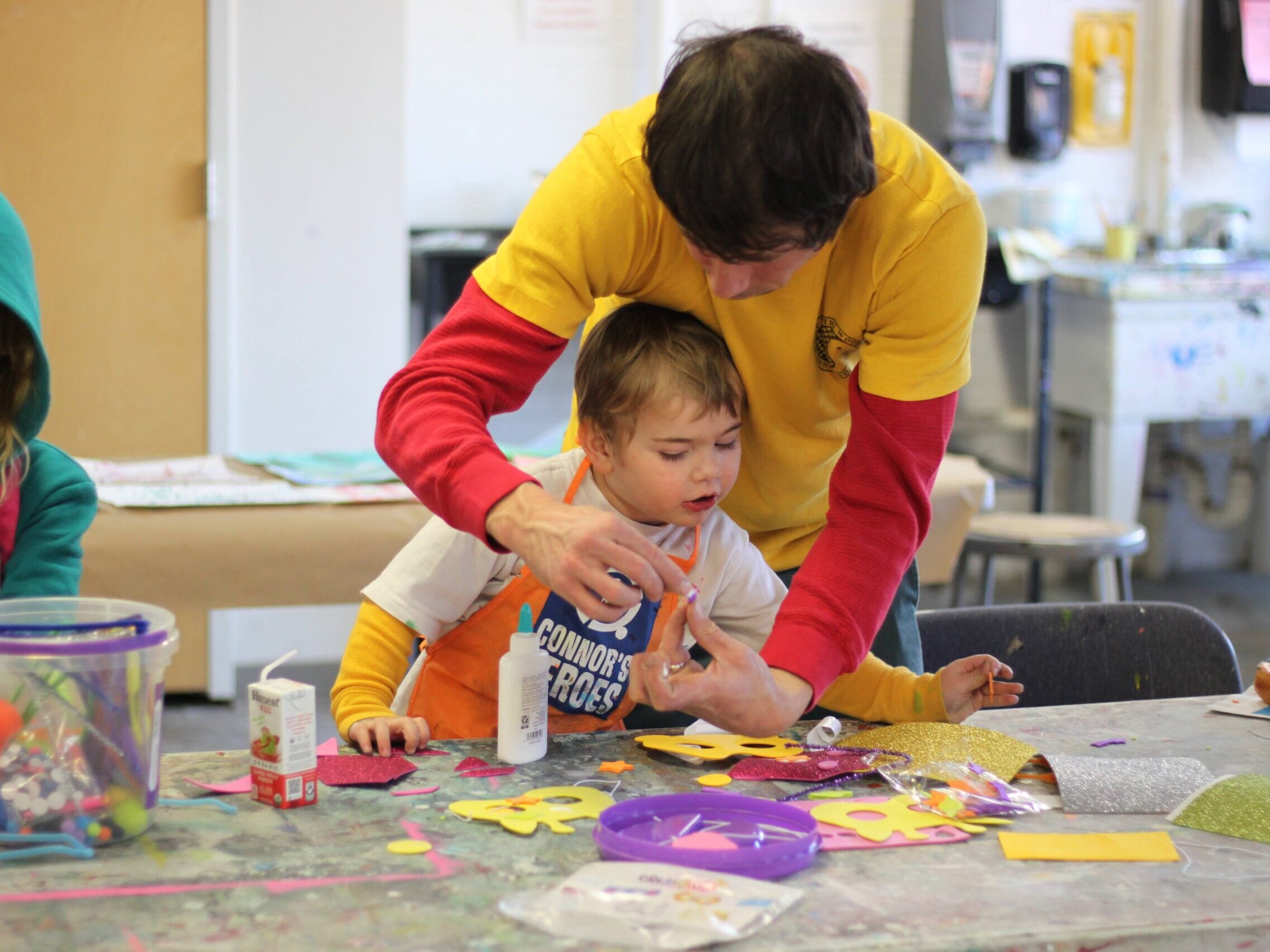 A dad has his arms around his son as they work on a craft project at Connor's Heroes Art Session