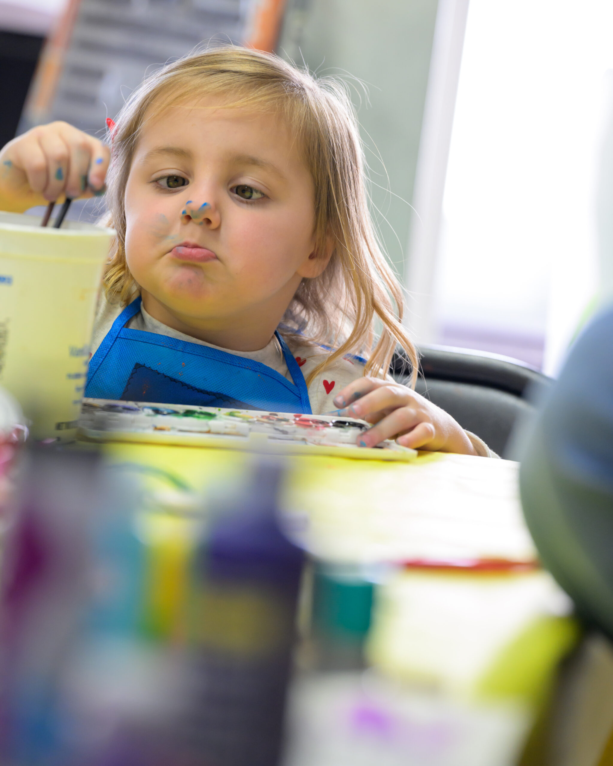 A girl with paint on her nose is in an art studio