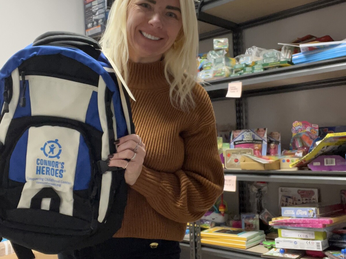 Brittany holds up a Connors Heroes backpack for a child with cancer