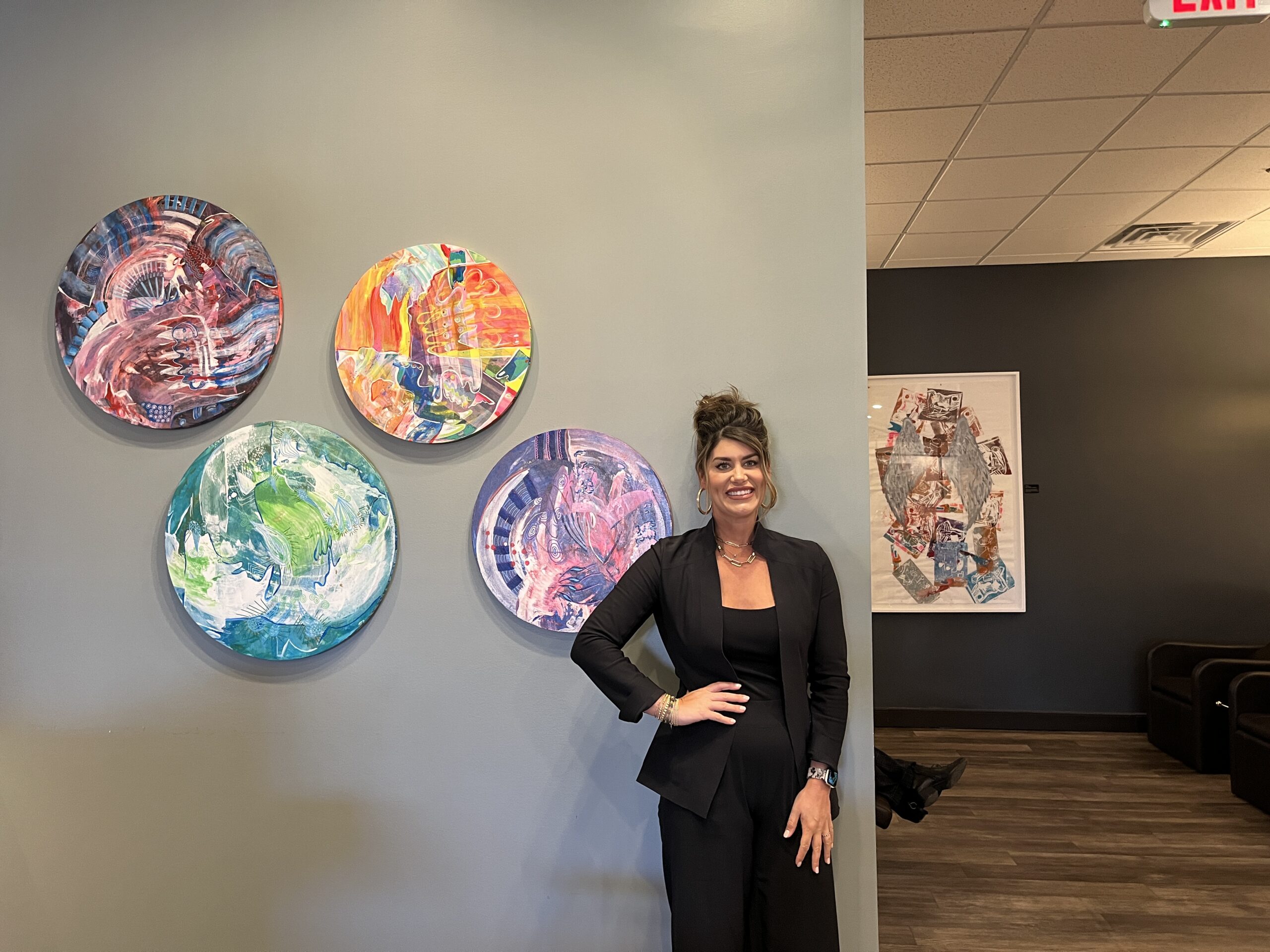 Rebekah stands in front of paintings in her salon