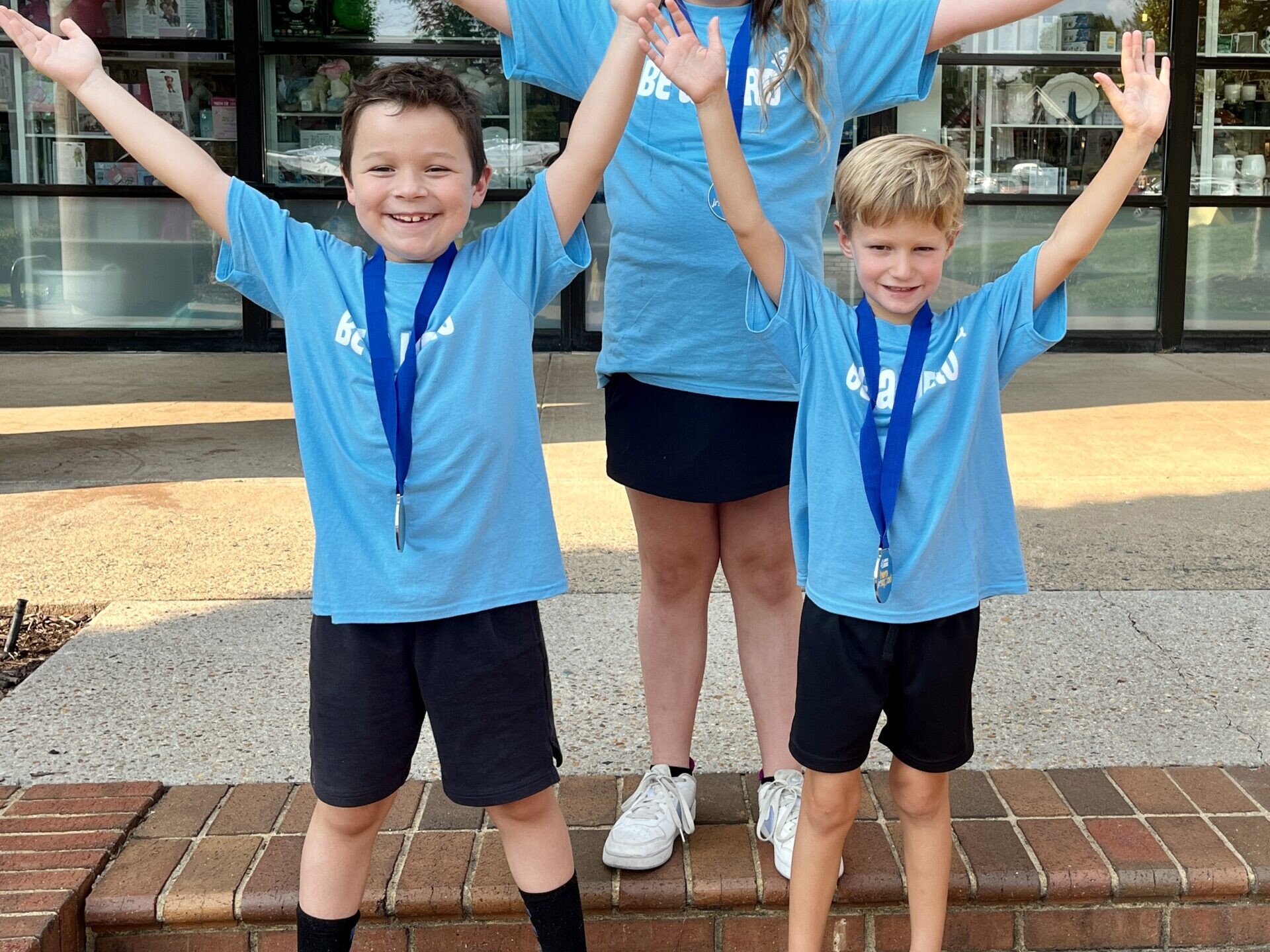 Three kids stand together with their hands up in the air