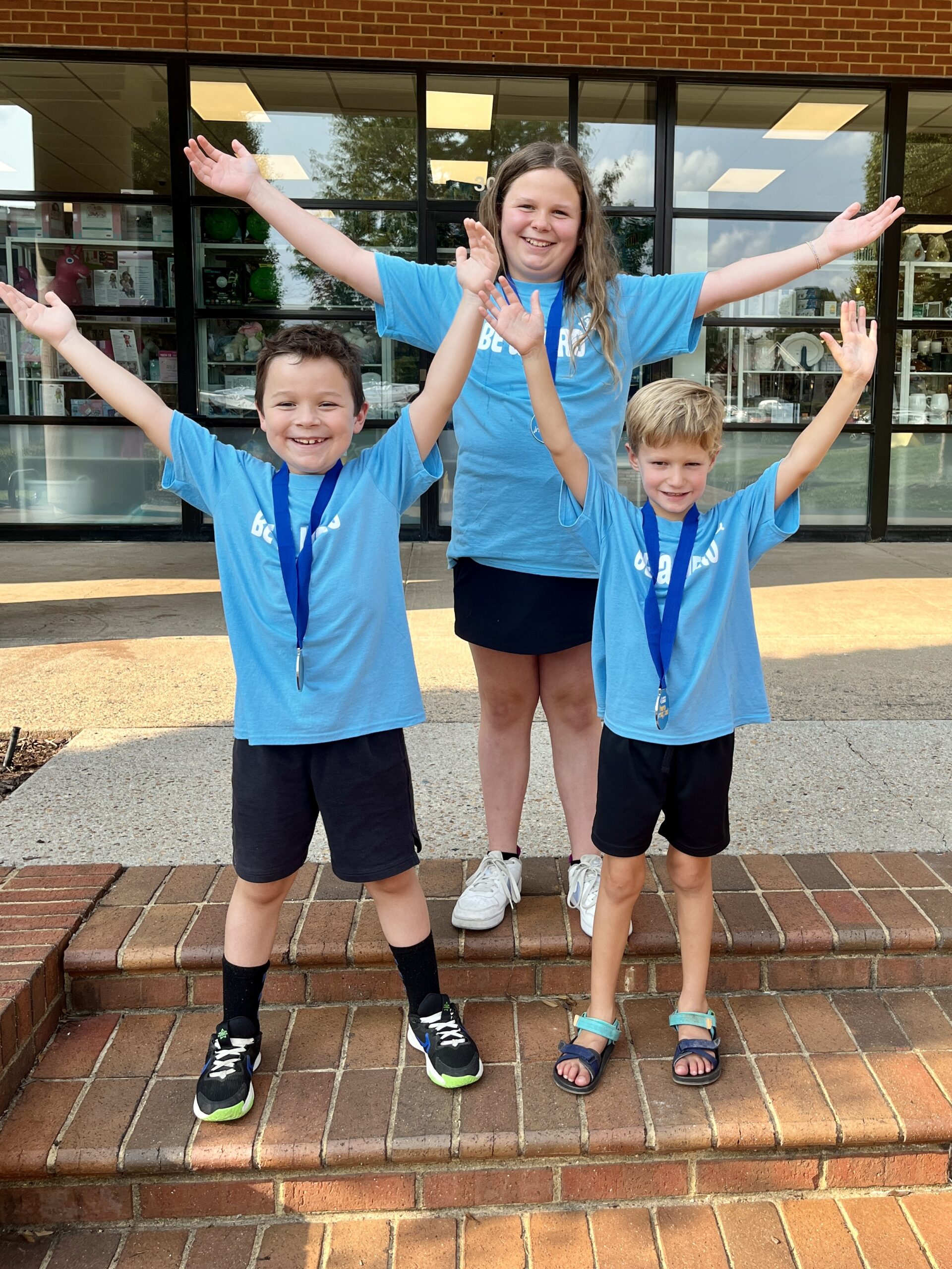 Three kids stand together with their hands up in the air